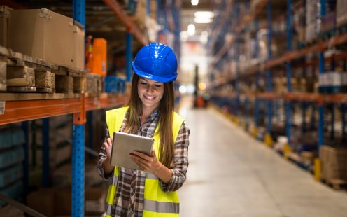 Warehouse female worker checking inventory on digital tablet in large distribution warehouse storage area.