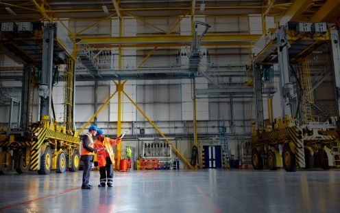 Shot of two warehouse workers talking together over a clipboard inside of a large warehouse