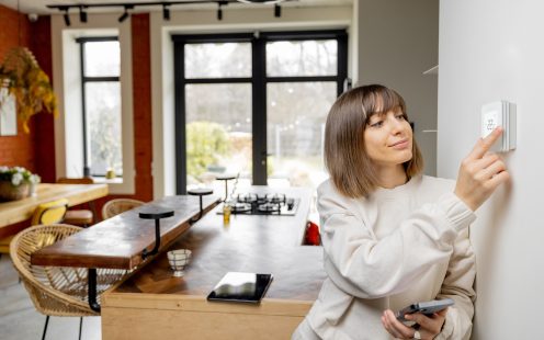 Woman controlling home temperature with electronic thermostat mounted on the wall in living room at home. Concept of modern technologies and smart home